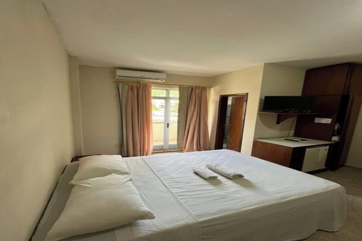 Una habitación de hotel con una cama, un escritorio con televisor y un equipo de aire acondicionado.