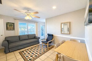 Ein Wohnzimmer mit Sofa, Esstisch, Stuhl, Deckenventilator und einem fensterbepflanzten Fenster.