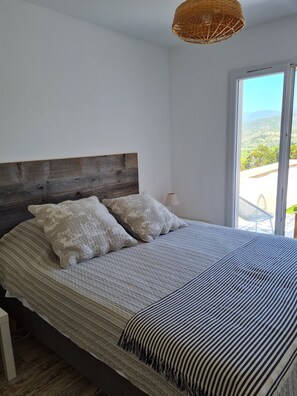 Ein Schlafzimmer mit Holzkopfteil, einem großen Bett mit gestreifter Bettwäsche und Blick durch eine Glastür.