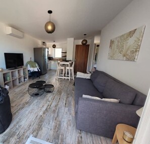 Ein Wohnzimmer mit grauem Sofa, einem Fernseher und einem Essbereich mit Tisch und Stühlen.