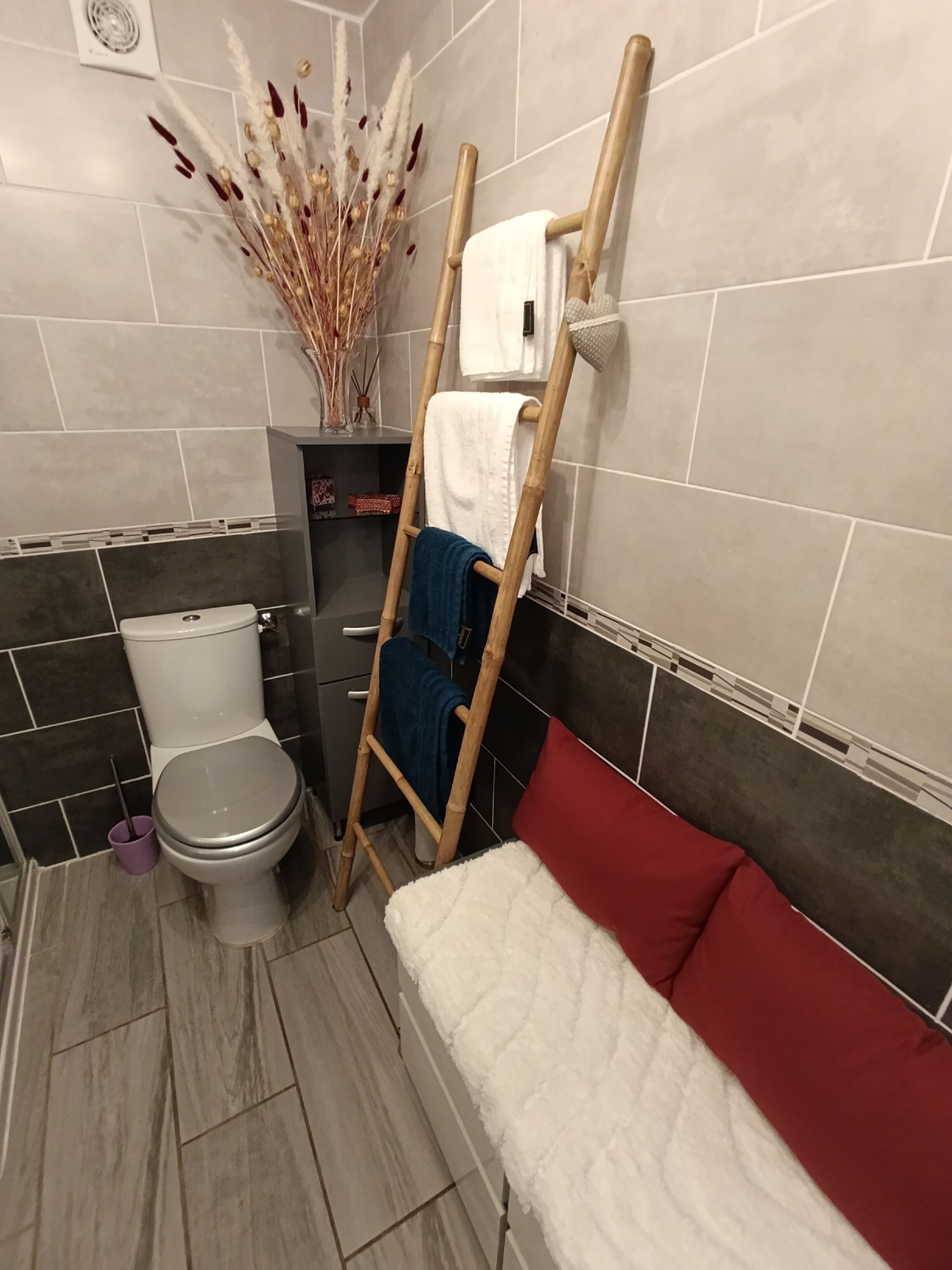 Een badkamer met een toilet, een houten trap, een witte handdoek, een rode kussen en decoratieve gedroogde planten.