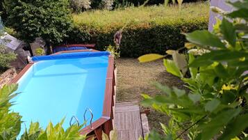 Una piscina con cubierta de madera, rodeada de abundante vegetación y vistas a una ladera boscosa.