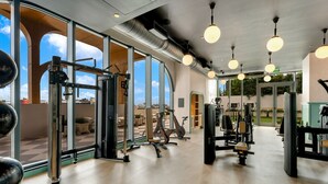 Ein Fitnessstudio mit unterschiedlichen Trainingsgeräten, großen Fenstern und Blick zum Himmel.