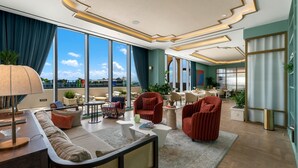 Ein geräumiger Wohnbereich mit einer Couch, Sesseln, einem Couchtisch und einem Essbereich mit Stühlen und Tischen. Große Fenster bieten Blick auf die Stadt.