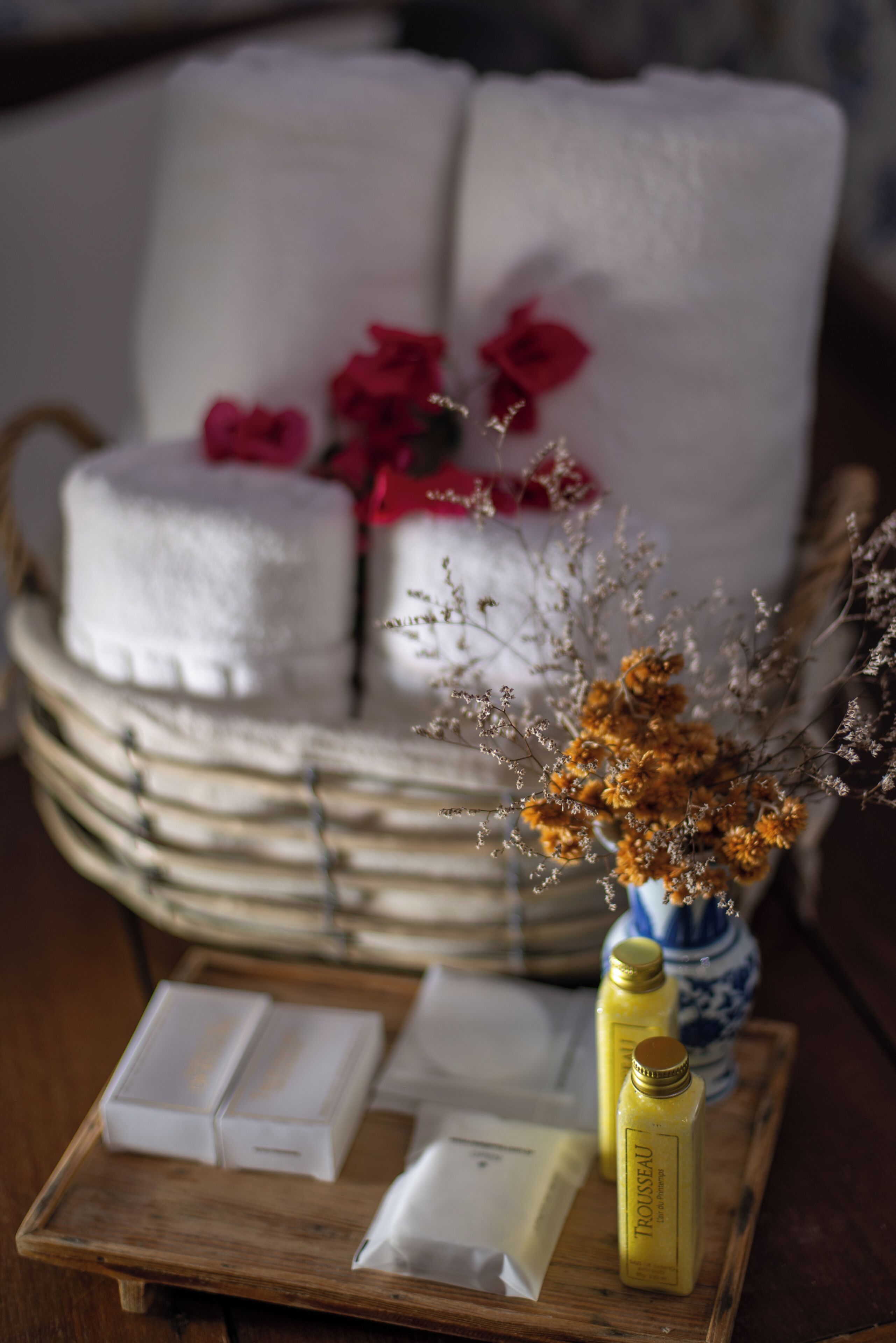Un plateau en bois contenant des articles de toilette, un vase avec des fleurs séchées et une pile de serviettes.
