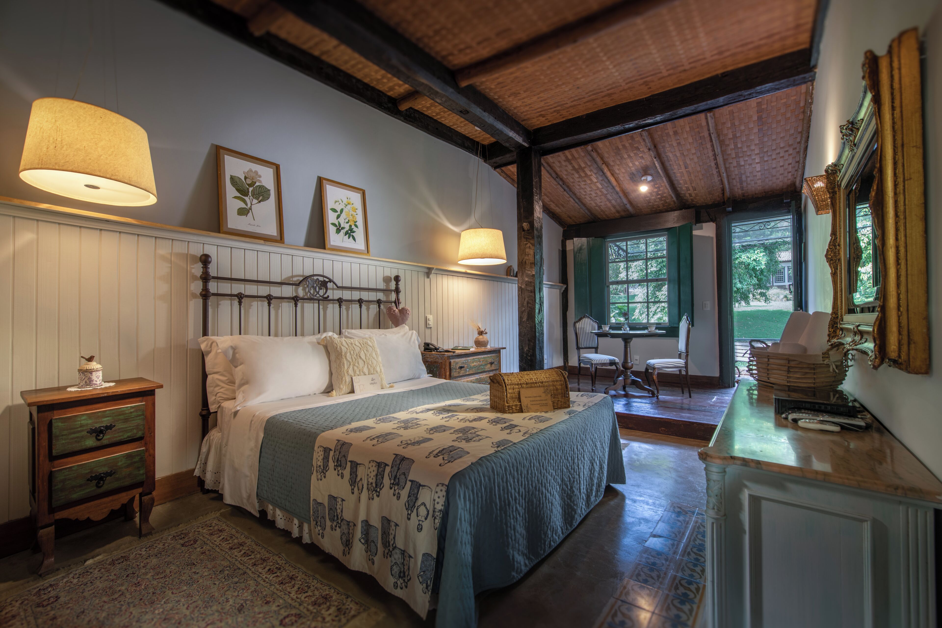 Quarto com cama, mesas de cabeceira, cômoda e janela com vista para o exterior.
