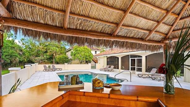 Un espace aménagé au bord de la piscine, avec un bar en bois, des chaises longues et un toit de chaume.