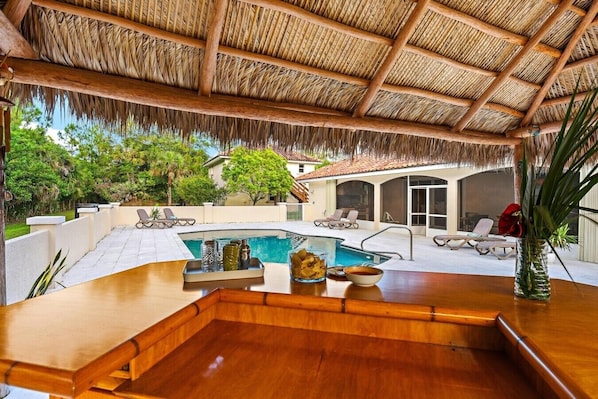 A poolside area with a wooden bar, lounge chairs, and a thatched roof.