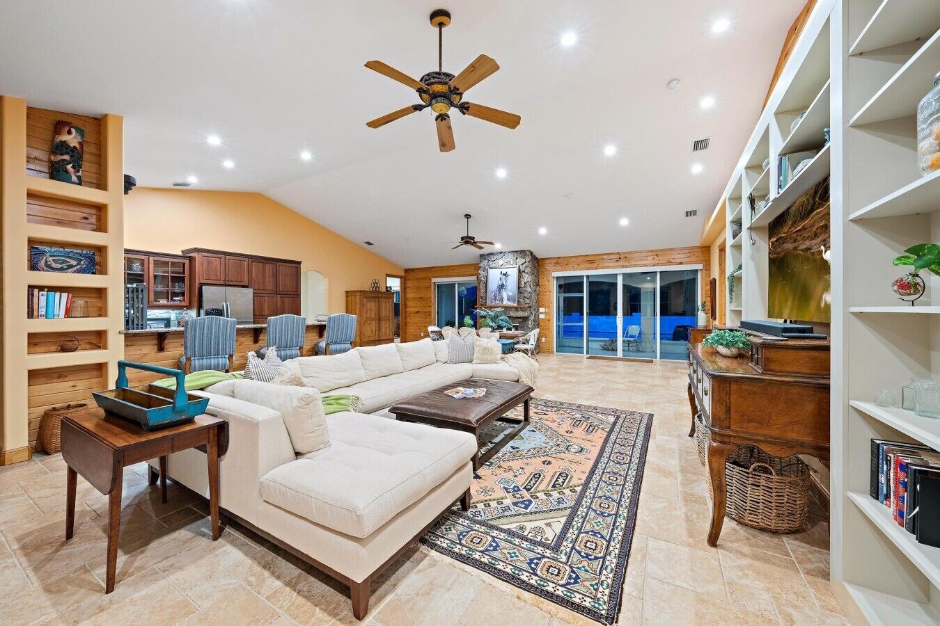 A spacious living room with a large sectional sofa, a ceiling fan, and a view of the backyard through sliding glass doors.
