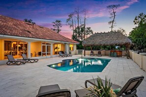 A swimming pool with lounge chairs, a bar area, and a thatched-roof structure.