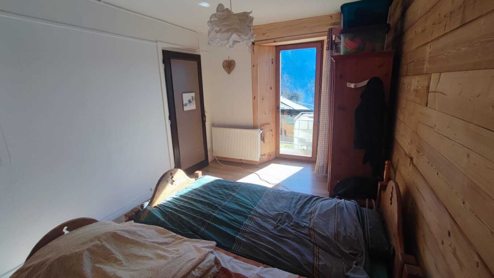 A small, cozy room with a bed, a wooden wardrobe, a radiator, and a view of the outside.