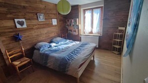 Una camera da letto con rivestimenti in legno, un letto, una sedia, un termosifone e una finestra con tende.