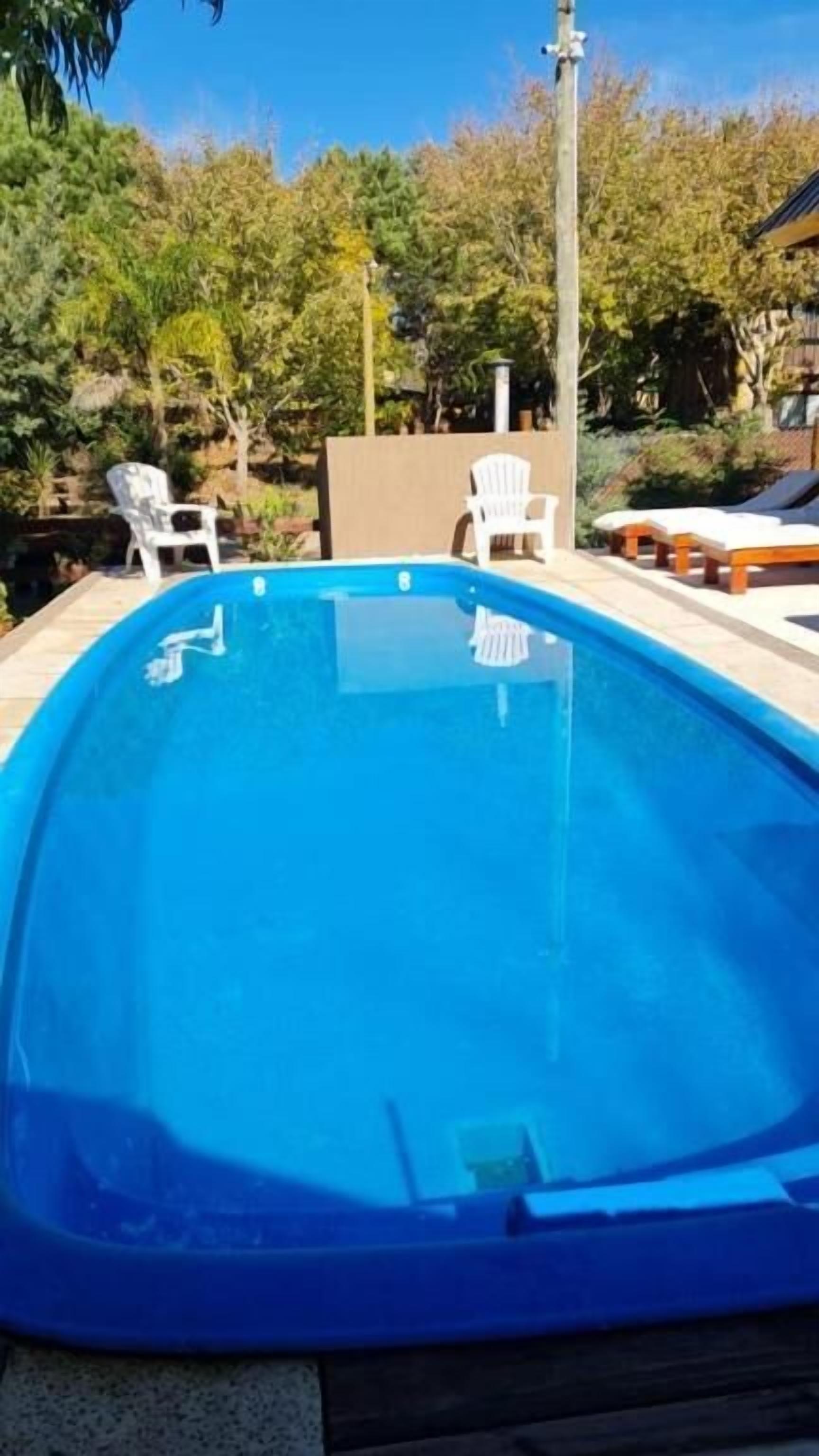 Una piscina con agua azul cristalina, rodeada de sillas de plástico blanco y una terraza de madera.