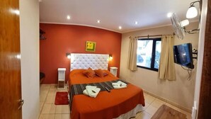 Una habitación de hotel con cama, televisión, escritorio y ventana con cortinas.