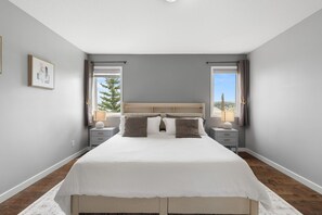 Ein Schlafzimmer mit einem großen Bett, zwei Nachttischen, einem Kopfteil und zwei mit Vorhängen versehenen Fenstern.