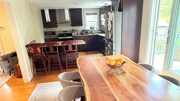 A modern kitchen with dark cabinetry, a wooden dining table, and a view of the outdoors. - October in Boston - Jamaica Plain Home Near Hospitals & New England Adventures (Boston)