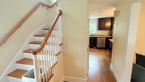 A staircase with wooden steps and white railings leading to an upper floor. A kitchen area is visible in the background with wooden cabinets and a dishwasher. - October in Boston - Jamaica Plain Home Near Hospitals & New England Adventures (Boston)