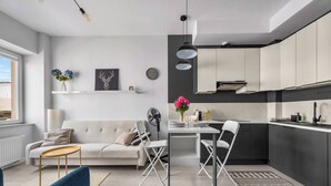 Uma cozinha moderna com armários brancos, uma mesa de jantar com cadeiras, um sofá e um ventilador.
