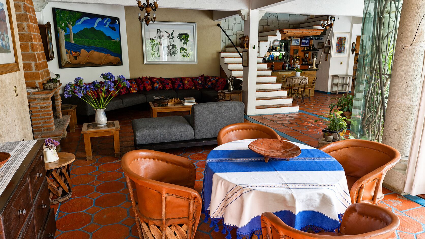 Una sala acogedora con sofá, sillones, una mesa con mantel azul y una escalera que conduce a una zona de bar.