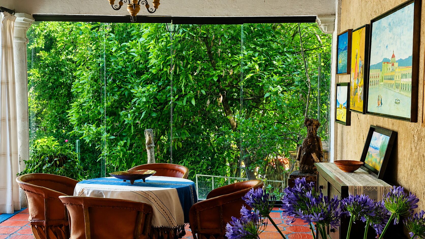 A room with a table and chairs, a statue, and a view of greenery through a window.