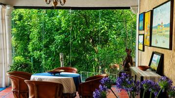 A room with a table and chairs, a statue, and a view of greenery through a window.