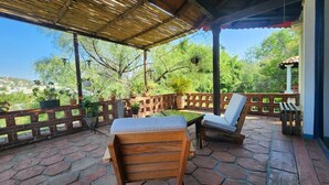Une terrasse couverte, aménagée avec des meubles en bois, des plantes en pot et offrant une vue sur le paysage environnant.