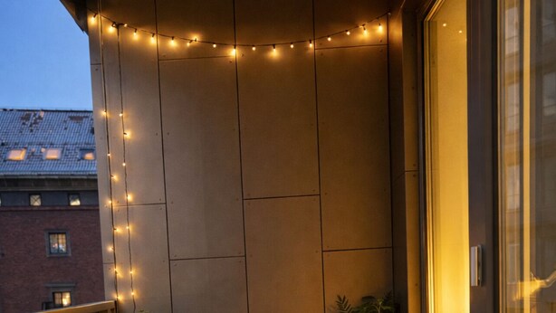 Un balcon avec une table et des chaises, des guirlandes lumineuses, des plantes en pot et un panier en osier.