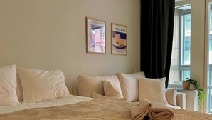 Une chambre d’hôtel avec un grand lit, deux tableaux encadrés au mur, une fenêtre avec des rideaux et une petite table sur laquelle est posée une plante.