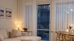 Une chambre à coucher comprenant un lit, un petit canapé, une table à manger avec des chaises, une fenêtre avec des rideaux et un mur orné de tableaux.