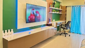 Uma sala de estar moderna com uma televisão grande fixada na parede, um armário de madeira embaixo e uma cortina azul na janela.