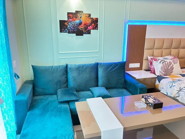 Una habitación de hotel moderna con un sofá azul, un cabecero de madera, un televisor de pantalla plana y un cuadro de un pavo real.