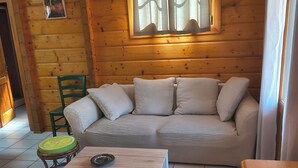 A log cabin interior with a beige sofa, a wooden coffee table, and a small stool. - Chalet near Mimizan in Bias in a holiday village 3KM from the ocean (Bias)