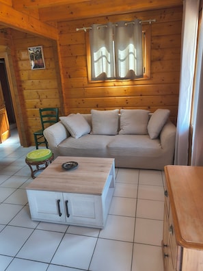 L’intérieur d’une cabane en rondins, avec un canapé beige, une table basse en bois et un petit tabouret.
