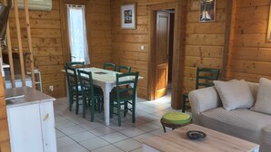 A log cabin interior with a dining table, chairs, a sofa, a small cabinet, and a tiled floor. - Chalet near Mimizan in Bias in a holiday village 3KM from the ocean (Bias)