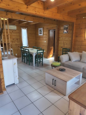 L’intérieur d’une cabane en rondins comprend une table à manger, des chaises, un canapé, un petit meuble et un sol carrelé.