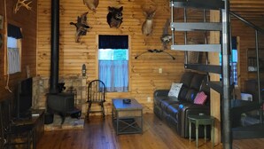 A cabin interior with a wooden interior, a fireplace, a spiral staircase, and various animal taxidermy mounted on the walls. - Mountain cabin on a creek and farm, 7 miles from Smoky Mountains National Park (Townsend)