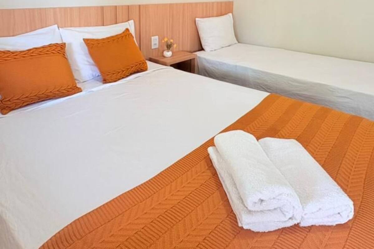A hotel room with a large bed, a smaller bed, and a nightstand with a vase.