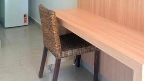 Quarto compacto com escrivaninha de madeira, uma cadeira, televisão de tela plana na parede e uma geladeira pequena.