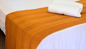 Quarto de hotel com uma cama, duas almofadas, uma mesa de cabeceira e uma toalha dobrada.