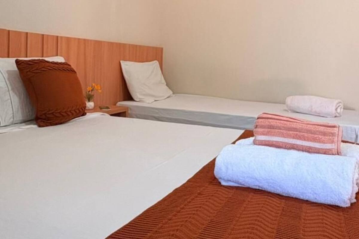 A hotel room with two beds, a wooden headboard, a wall-mounted air conditioner, and a small table with a vase of flowers.