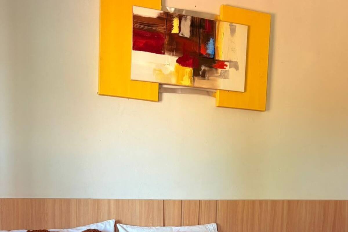 A hotel room with a large bed, brown and white bedding, a wooden headboard, a nightstand with a vase of flowers, and a painting on the wall.