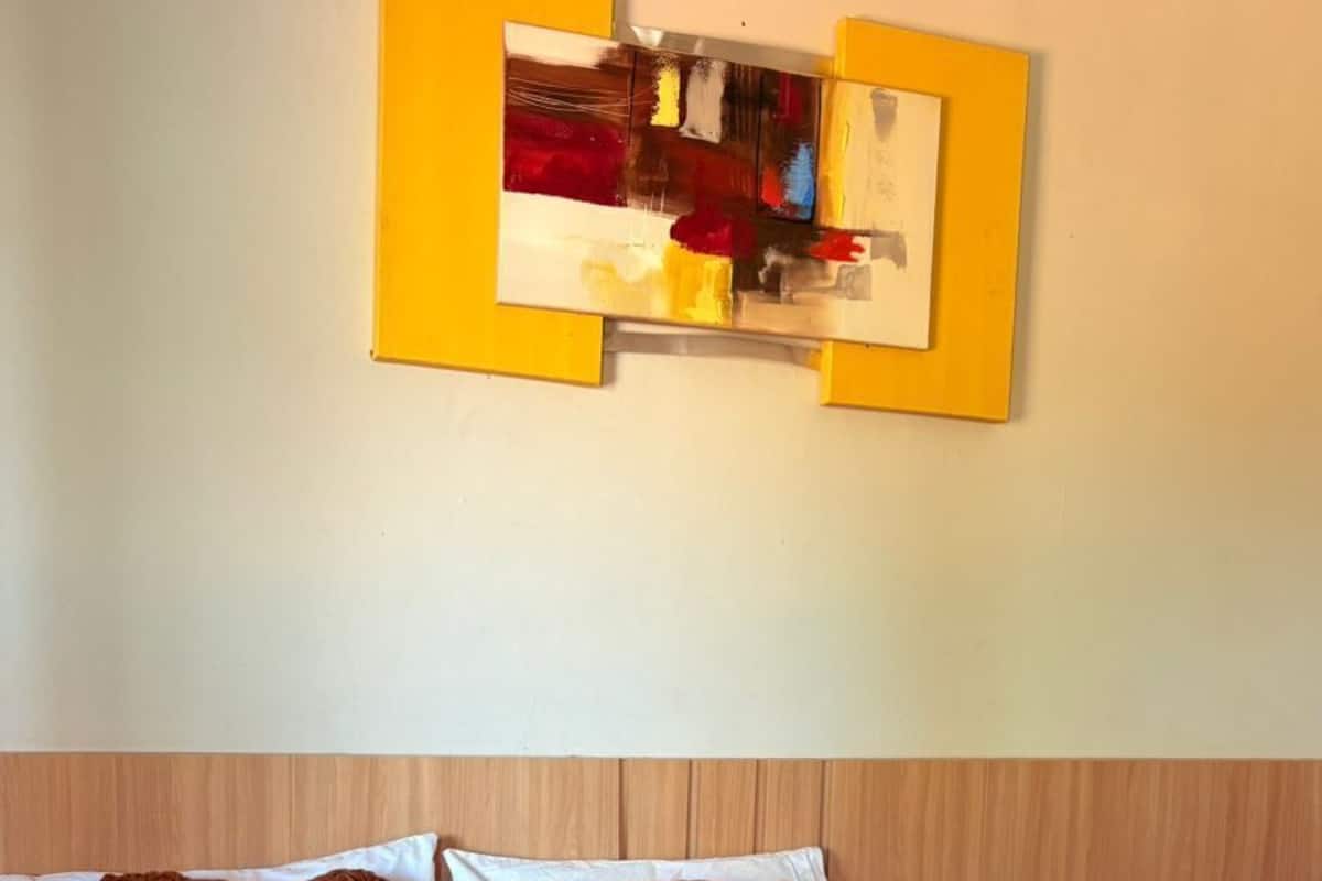 A hotel room with a large bed, brown and white bedding, a wooden headboard, a nightstand with a vase of flowers, and a painting on the wall.
