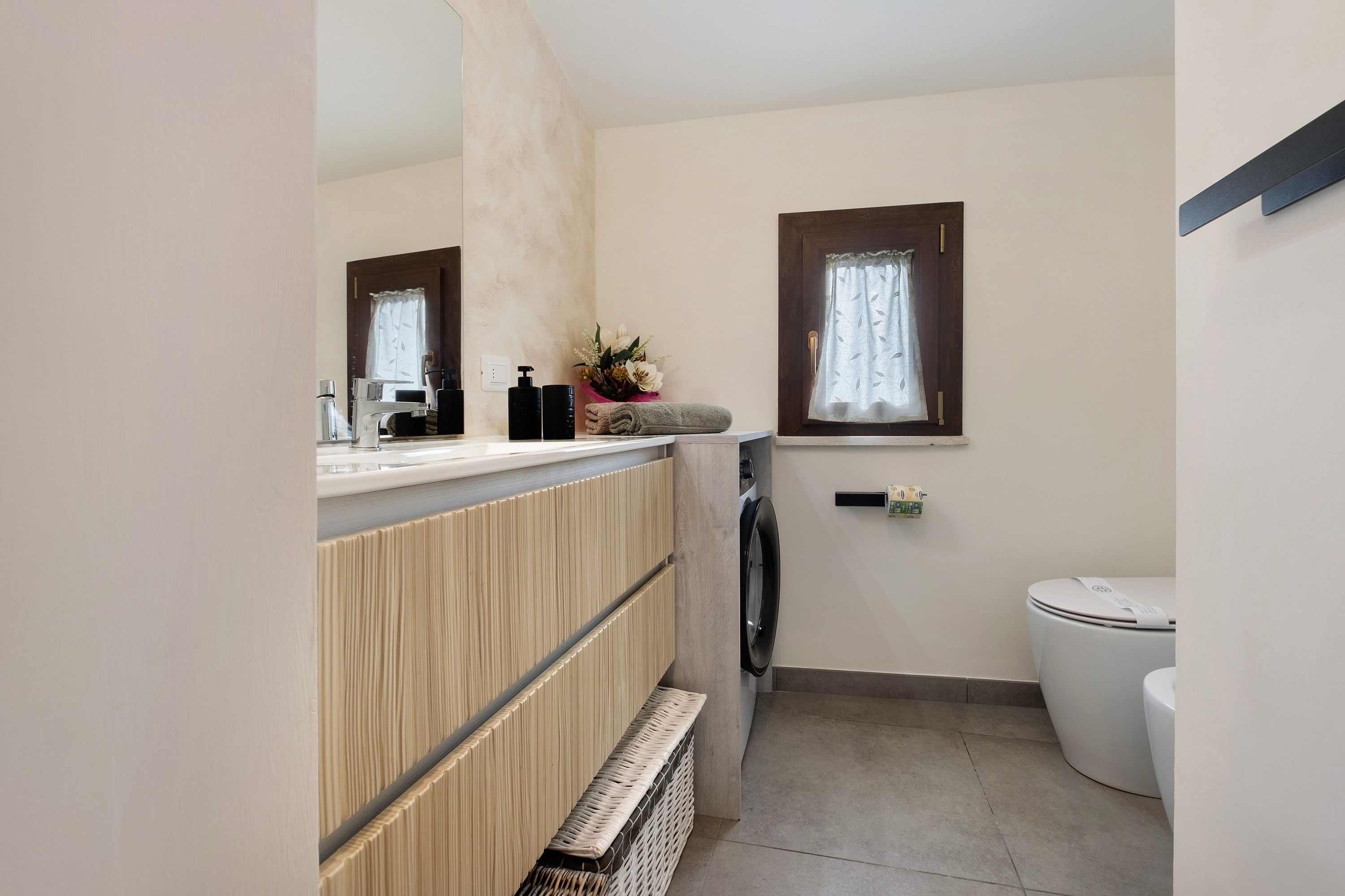 Een kleine badkamer met een wastafel, spiegel, toilet en een klein raam.