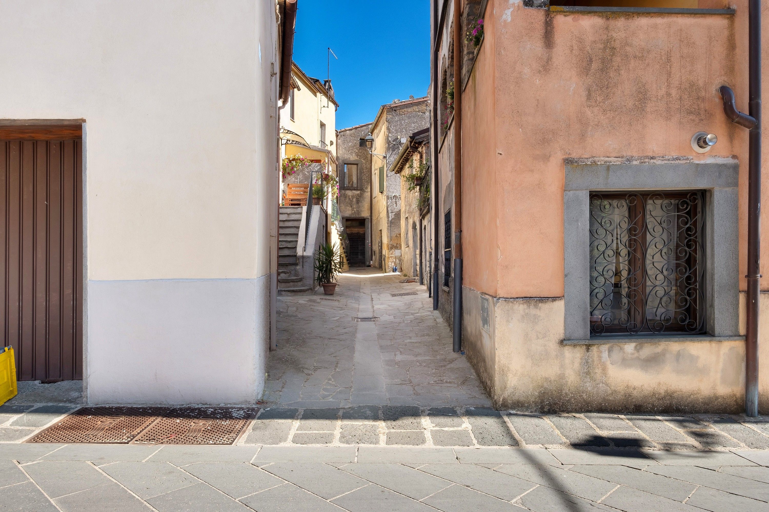 A narrow street with buildings on either side, a clear sky, and a door on the left.