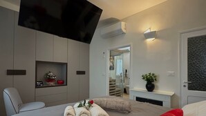 Ett modernt hotellrum med en stor säng, en platt-TV som är monterad på väggen, ett litet nattduksbord med en växt och en spegel ovanför dörren.