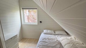 A small, sloped ceiling room with a bed, a window, and a dresser.