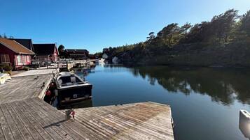 A wooden dock extending into calm water with boats docked, surrounded by trees and buildings.