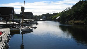 A calm river with boats docked at a wooden pier, surrounded by houses and greenery.