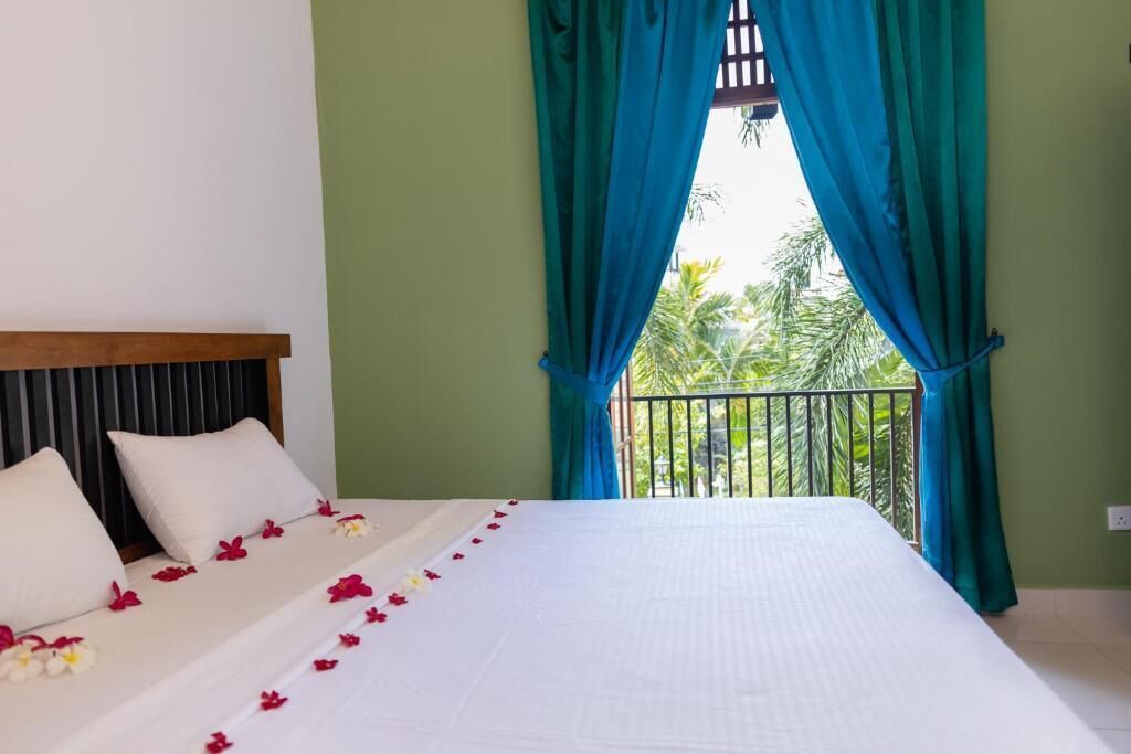 Habitación de hotel con cama, paredes verdes y balcón con vista a palmeras.