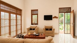 A living room with a sofa, two armchairs, a coffee table, a TV, and sliding doors leading to a garden. - Seahorse Villas - Three-Bedroom Apartment (NEGOMBO)
